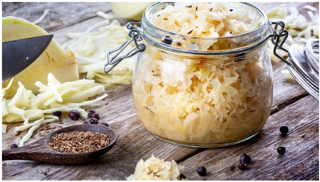 Ein Glas mit Sauerkraut, geschnittenem Kohl, Gewürzen und einem Löffel auf einem rustikalen Holztisch