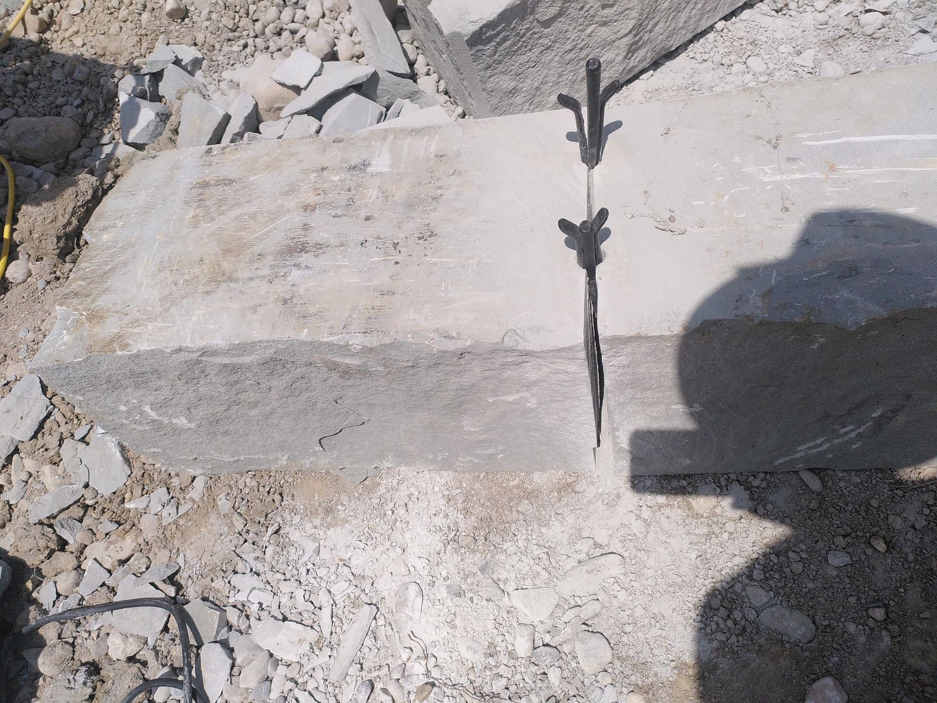 Zerbrochener Betonweg neben Trümmern, im hellen Sonnenlicht der Schatten einer Person.