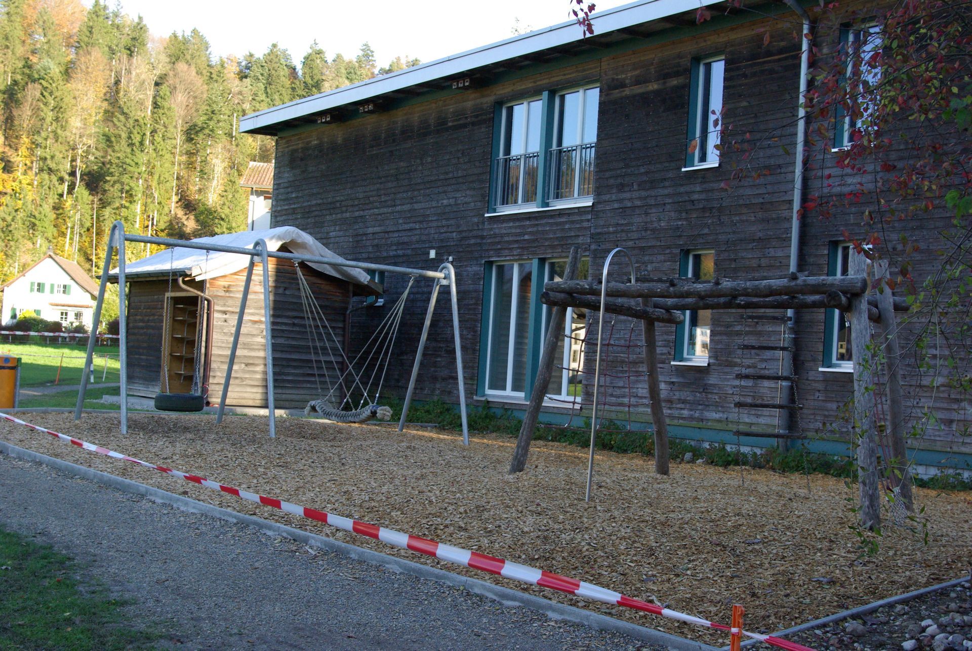 Backsteingebäude mit kleinem Spielgerät und Netzrahmen neben einem rot-weissen Bordstein, im Freien in einem Waldgebiet