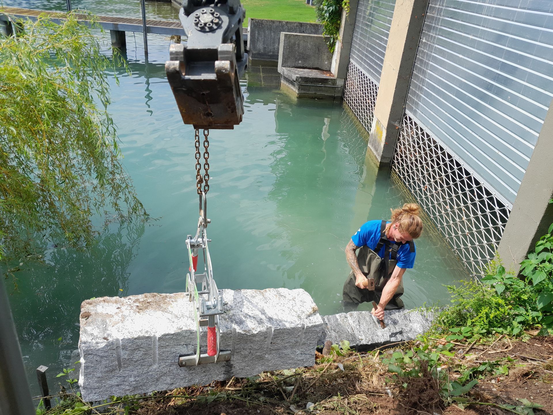 Ein Arbeiter hockt neben einem Kanal, während ein Kran einen Betonblock ins Wasser hinablässt.