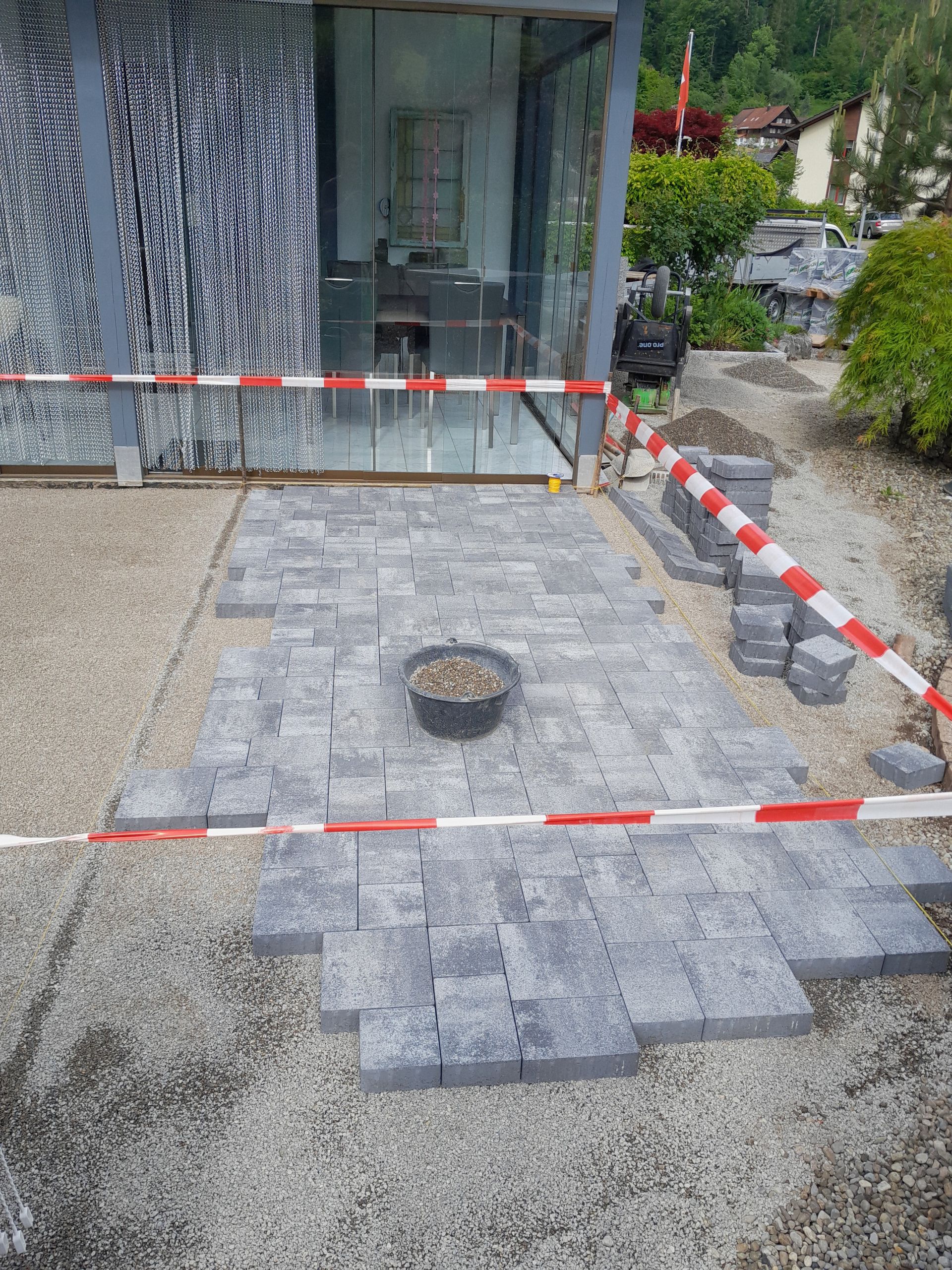 Abgesperrter Bereich für die Reparatur einer grauen Pflasterterrasse vor dem Eingang eines Glasgebäudes