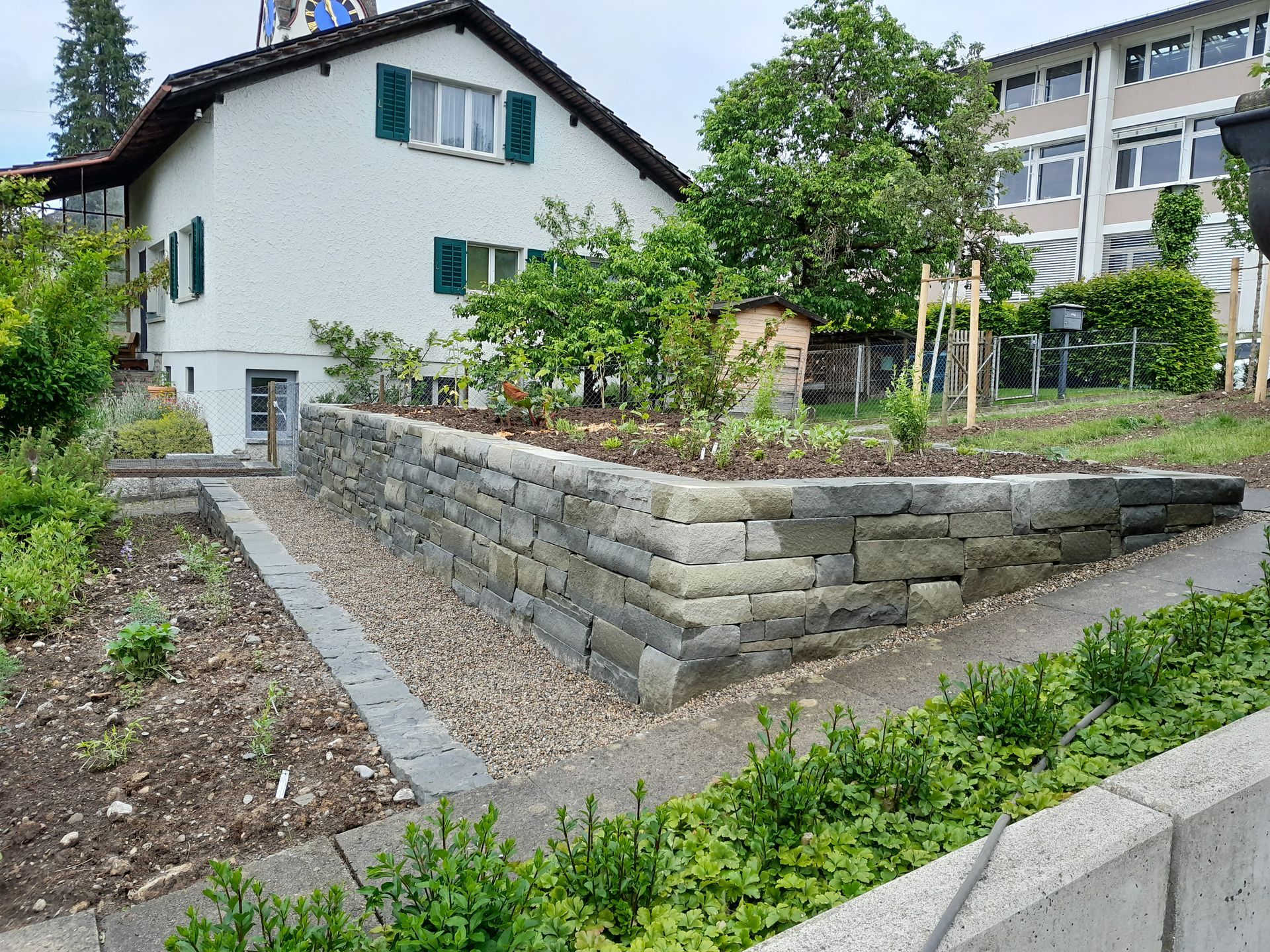 Ein terrassenförmig angelegter Steingartenweg neben einem weissen Haus und grünen Sträuchern in einem Wohngarten