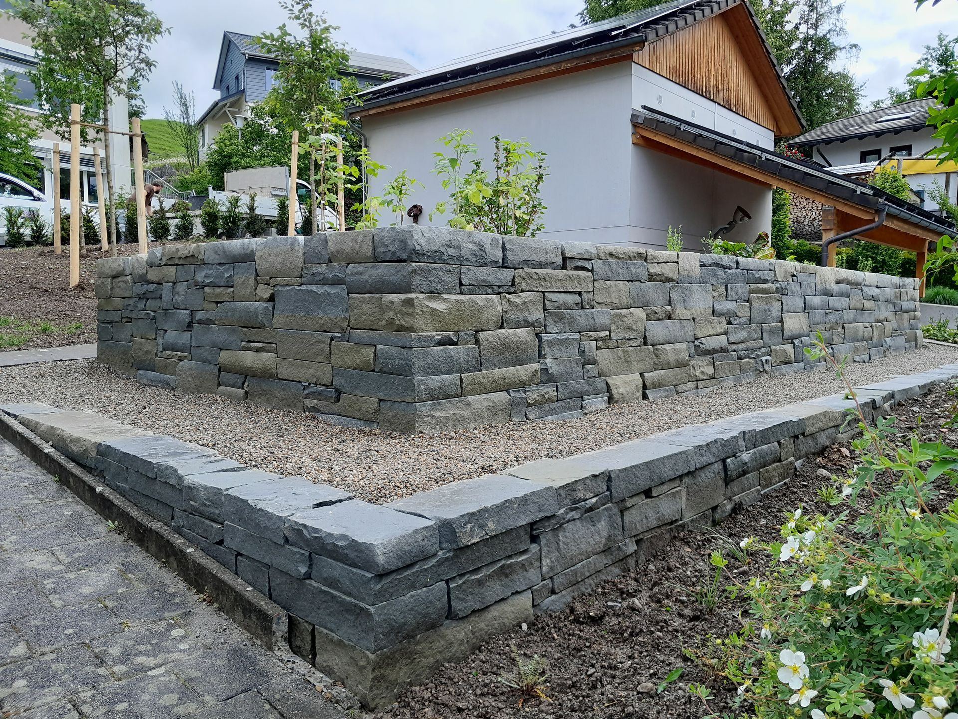 Terrassenförmige Steinstützmauer neben einem modernen Haus und einem angelegten Gartenweg