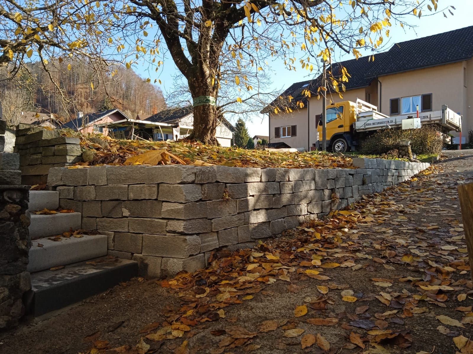 Steinmauer neben laubbedecktem Hof und Haus im Herbst
