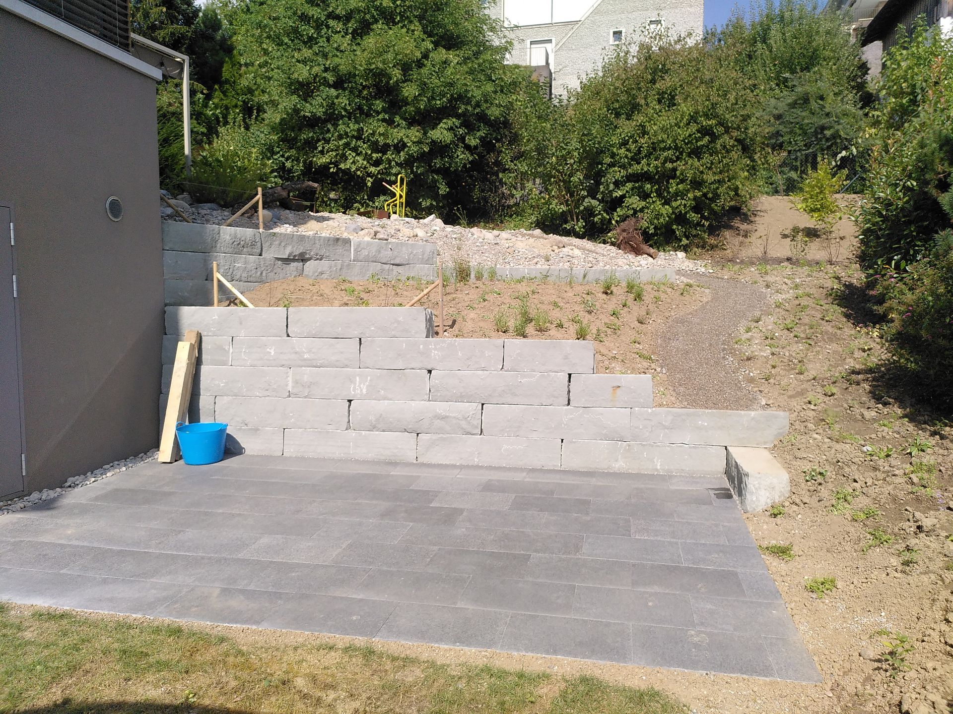 Hinterhofterrasse mit Betonstufen, einem blauen Eimer und einem abfallenden Gartenhang