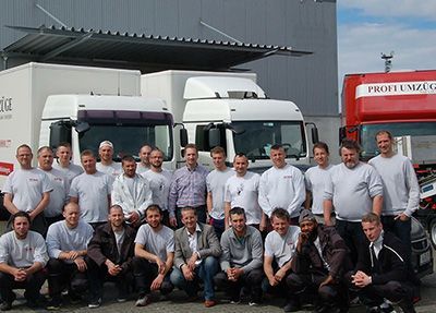 Eine Gruppe Männer posiert vor Lastwagen für ein Foto.