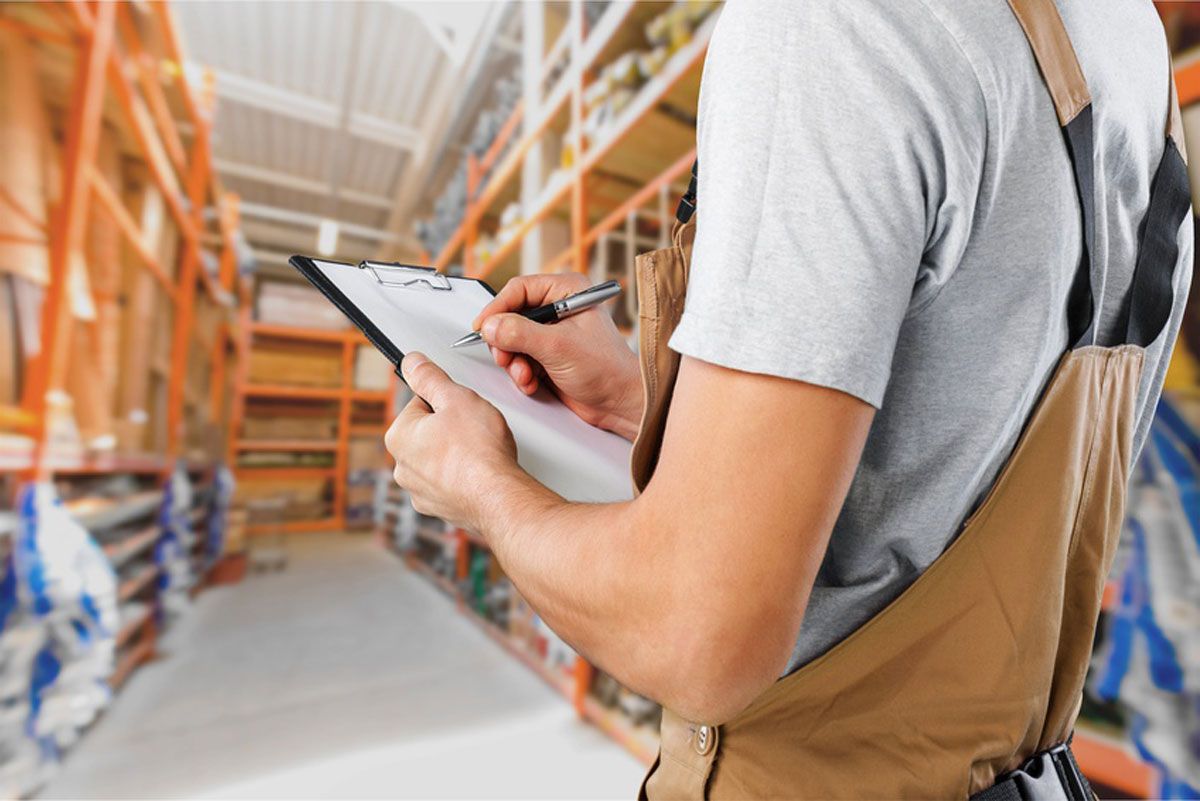 Ein Mann schreibt in einem Lagerhaus auf einem Klemmbrett