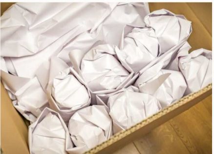 Ein mit weißem Geschenkpapier gefüllter Karton auf einem Holzboden.