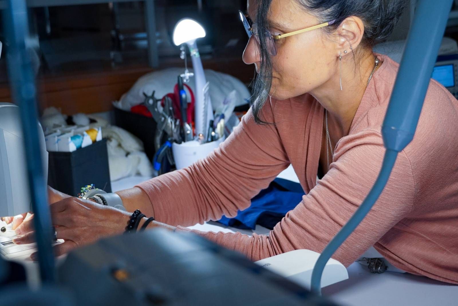 Eine Frau mit Brille sitzt an einem Tisch und arbeitet an einer Maschine.