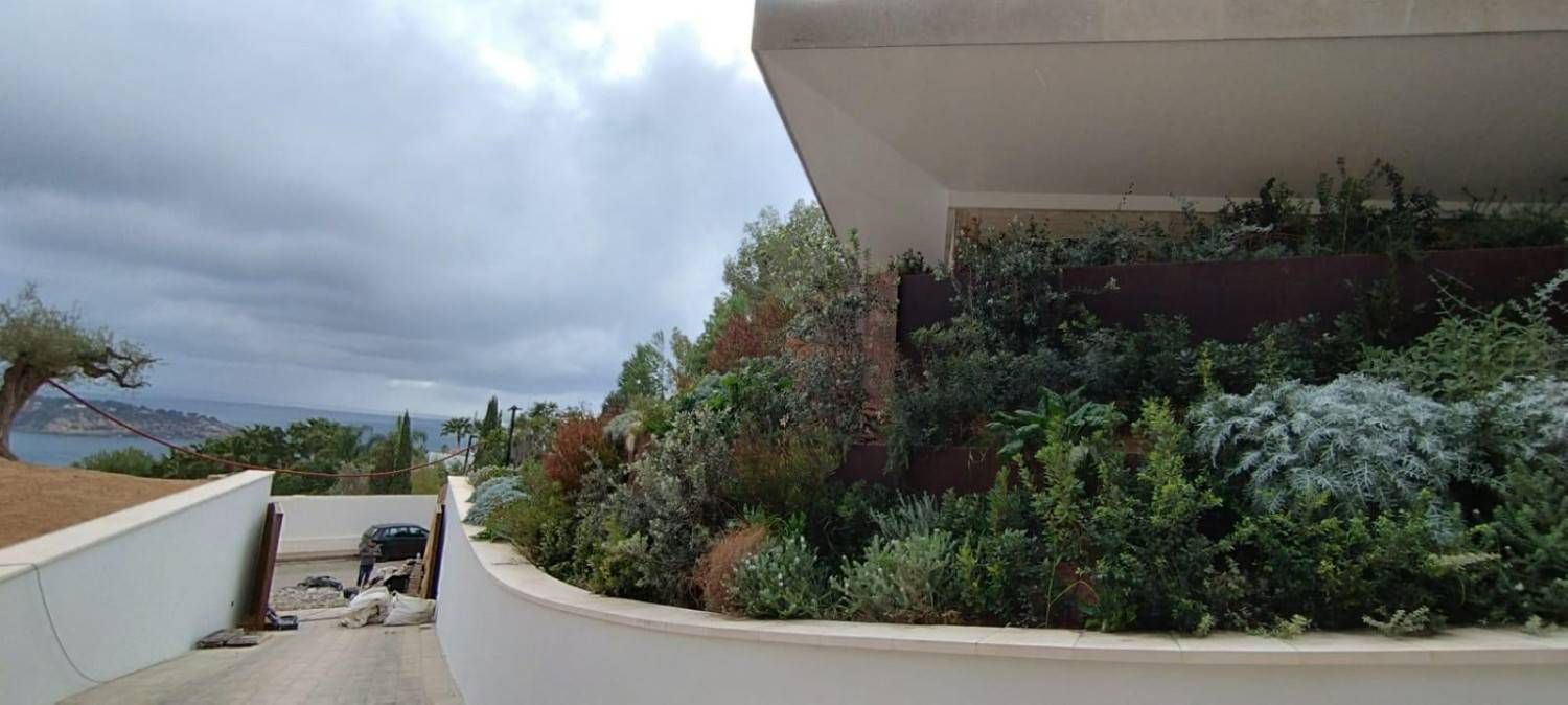 Un edificio moderno con una pared curva y un jardín en la azotea con vista a un océano nublado.