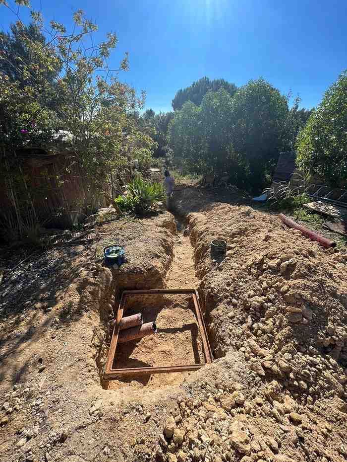 Una zanja cavada en un patio trasero, enmarcando un área cuadrada con ladrillos, con herramientas
