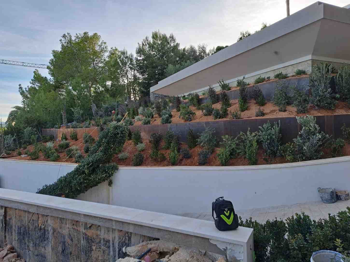 Casa moderna con terrazas y exuberante vegetación. Una mochila reposa en la pared.