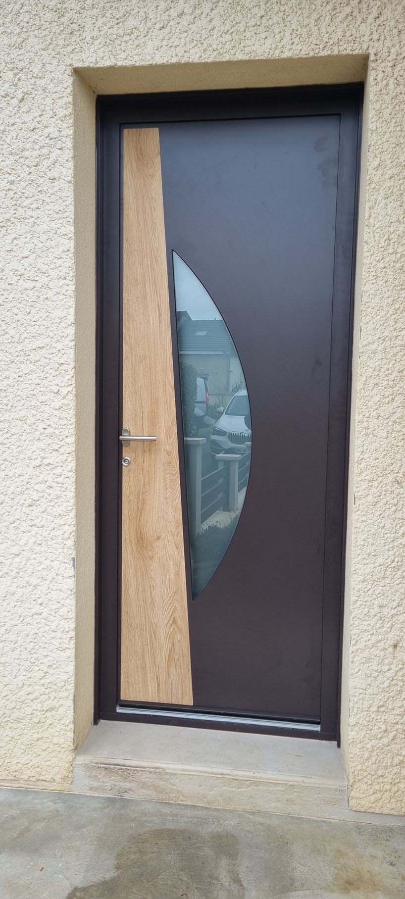 Porte grise avec vitrage décoratif, encastrée dans un cadre en pierre, des marches mènent à la porte.