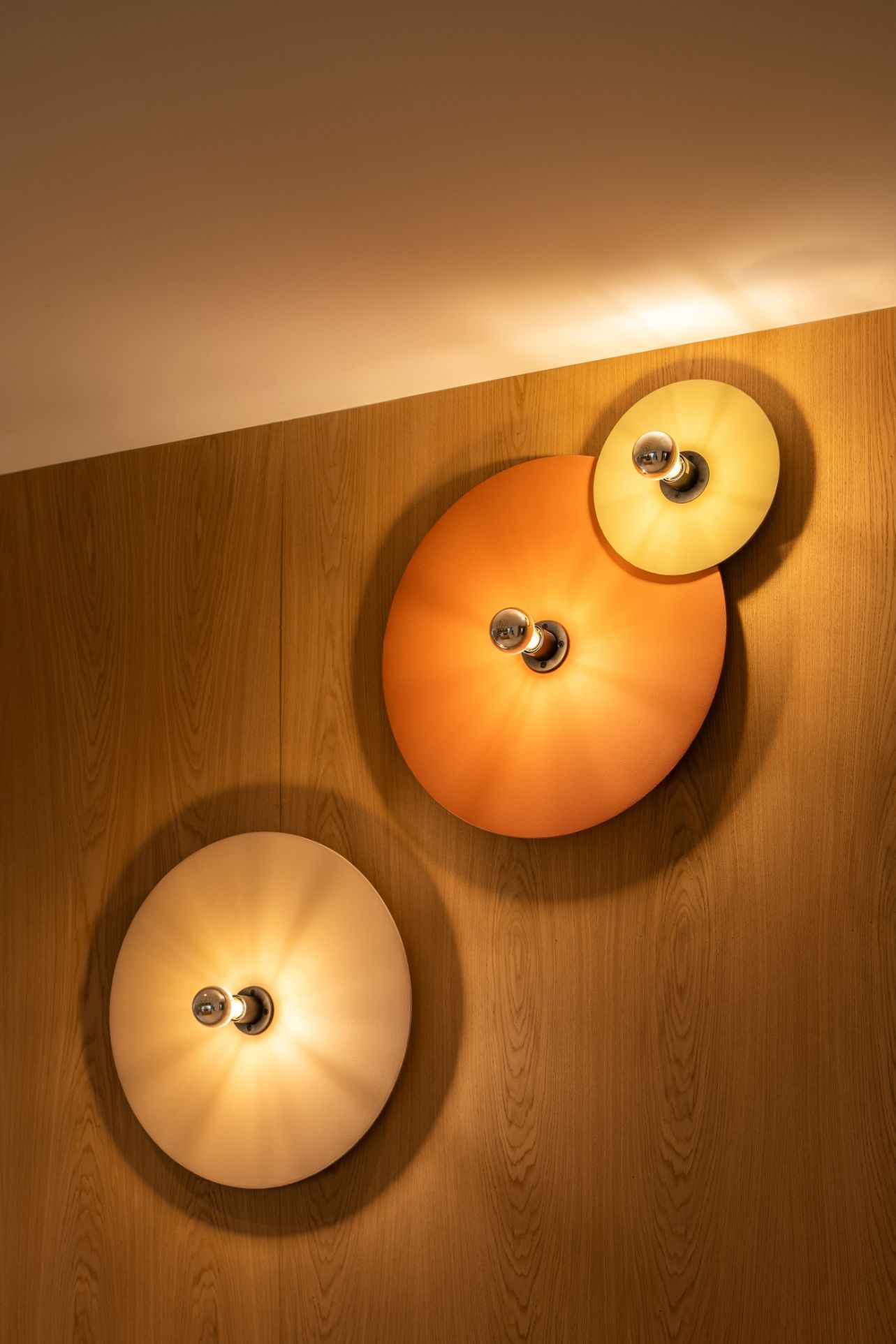 Tres apliques de pared con forma de disco que emiten una luz cálida y brillante, montados sobre un panel de madera vertical.