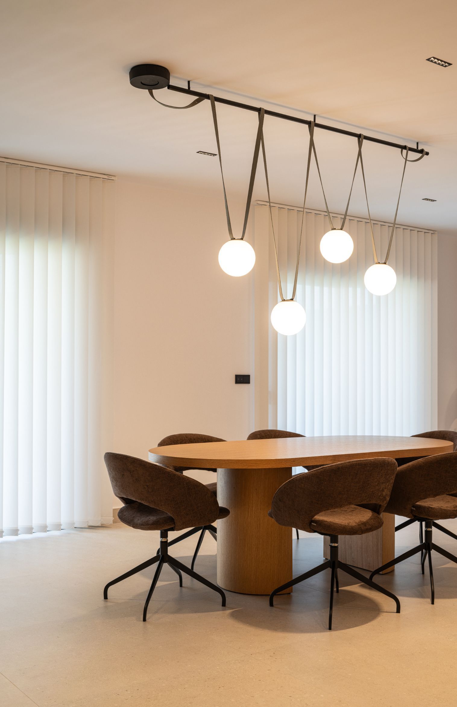 Un comedor moderno con una mesa ovalada de madera, sillas tapizadas y una lámpara colgante de cuatro globos