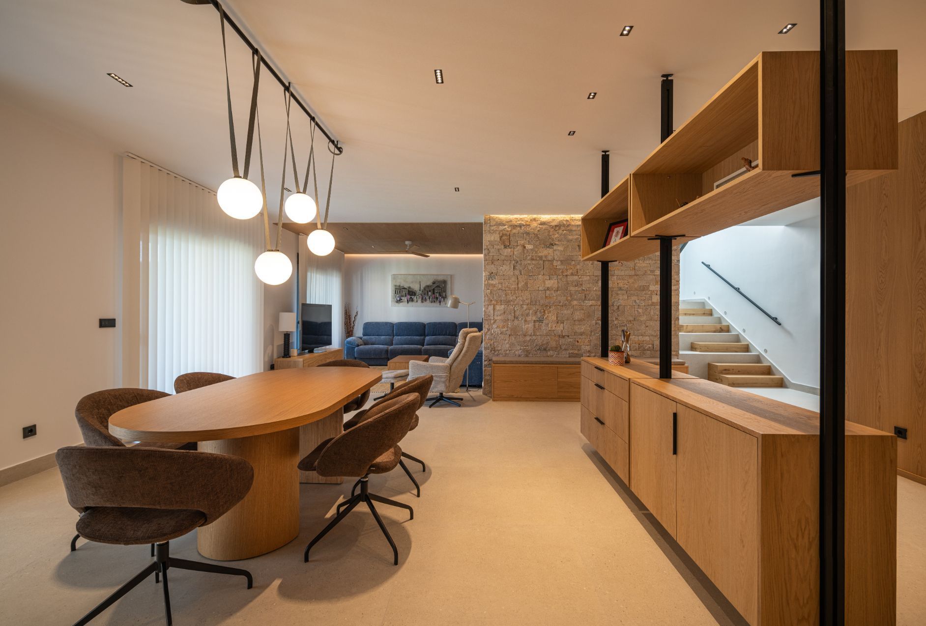 Un moderno espacio diáfano que integra salón y comedor, con mesa de madera, sillas marrones, estanterías a medida 