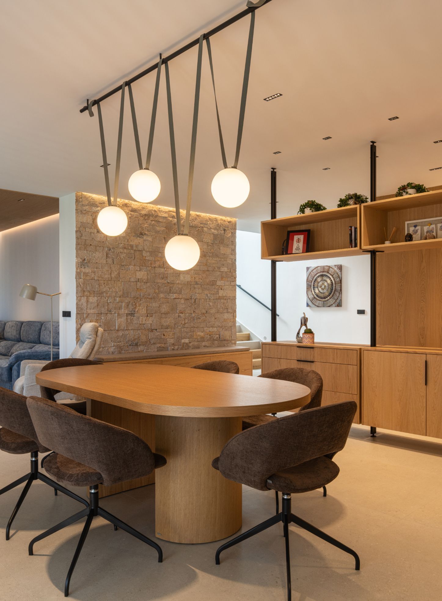 Un comedor moderno con una mesa ovalada de madera, sillas giratorias oscuras y una lámpara colgante con cuatro globos 