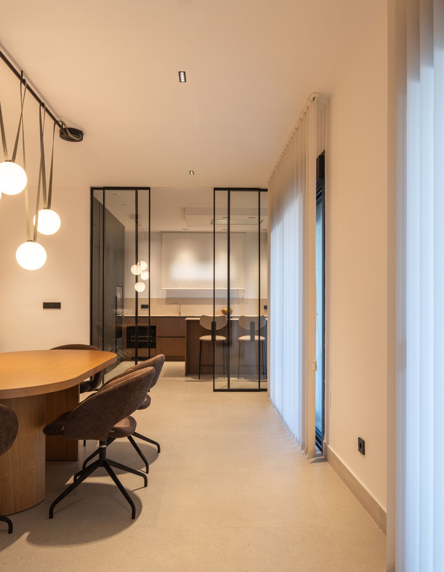 Un moderno comedor con una mesa redonda de madera, lámparas colgantes esféricas y vistas a la cocina