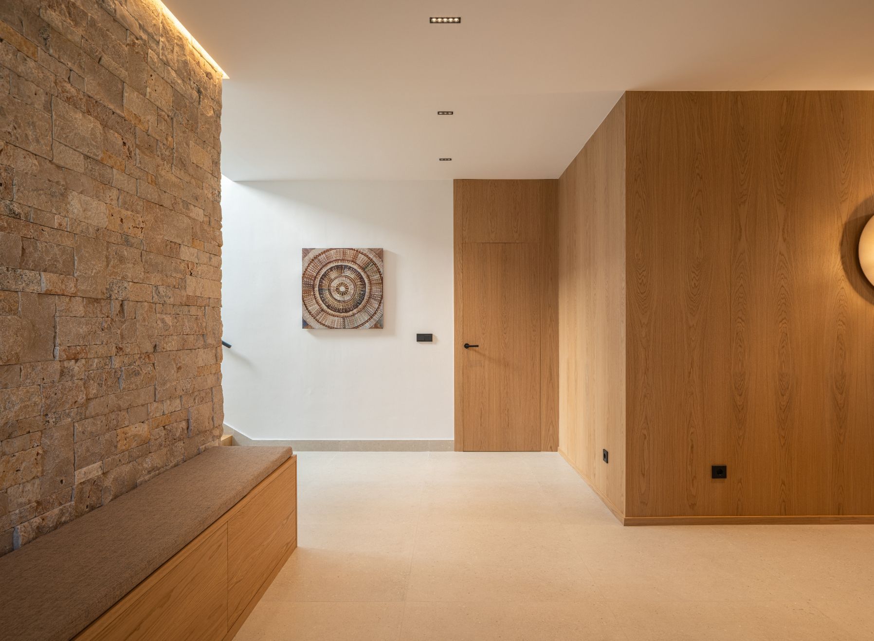 Pasillo minimalista con pared de piedra texturizada, banco empotrado de madera, revestimiento de madera clara