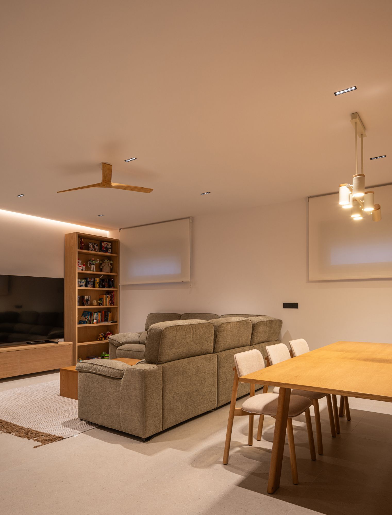 Una sala de estar moderna con un sofá modular gris, un juego de comedor de madera clara, una estantería