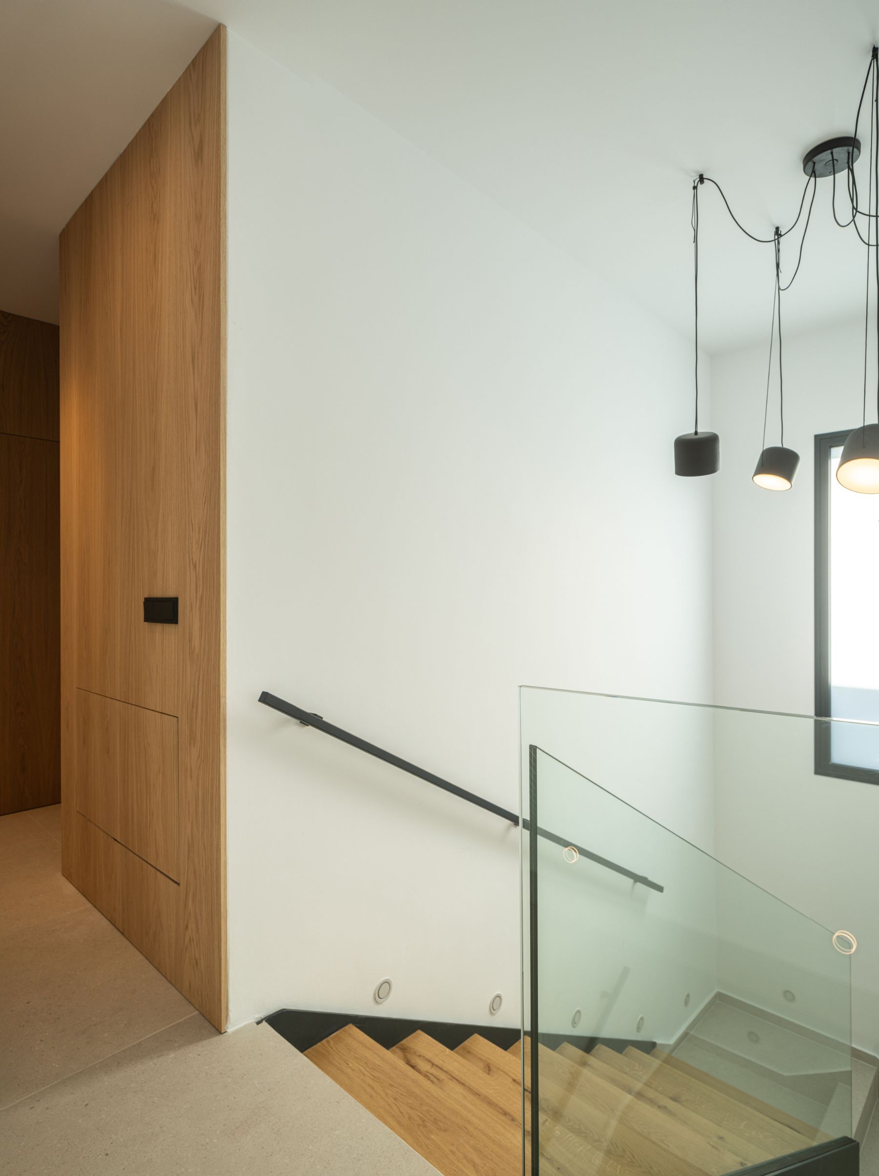 Escalera moderna con peldaños de madera, barandilla de cristal, pasamanos negro y una pared decorativa 