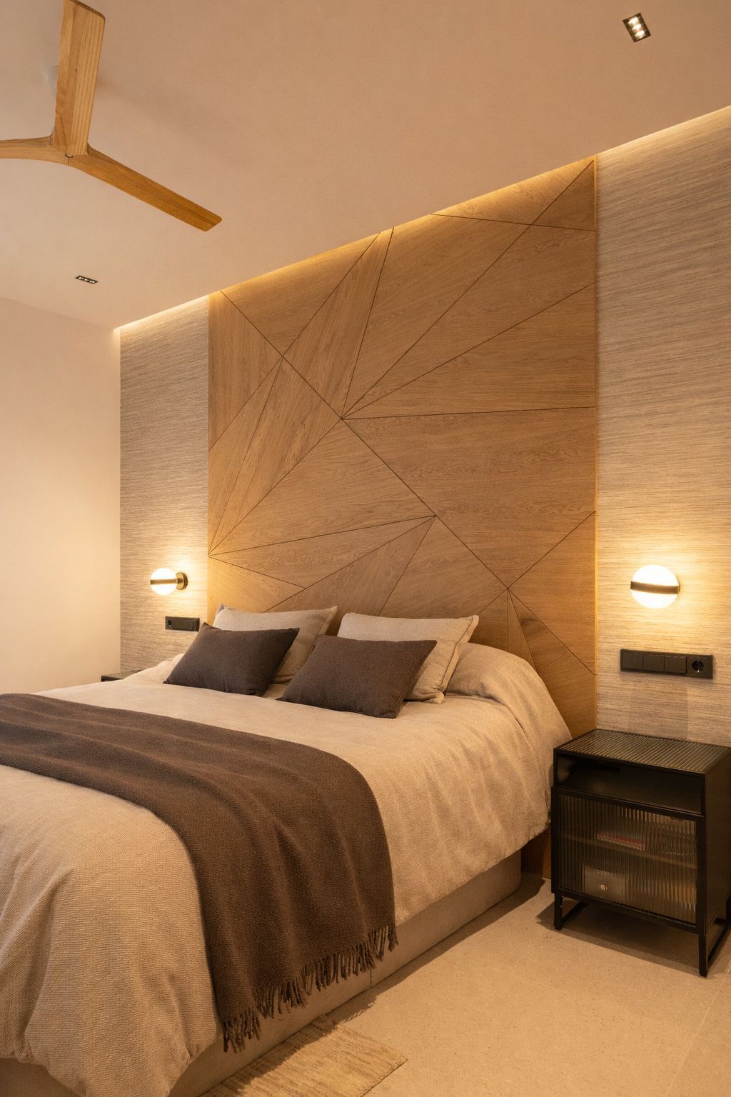 Un dormitorio moderno con cabecero de madera con paneles geométricos, iluminación ambiental cálida
