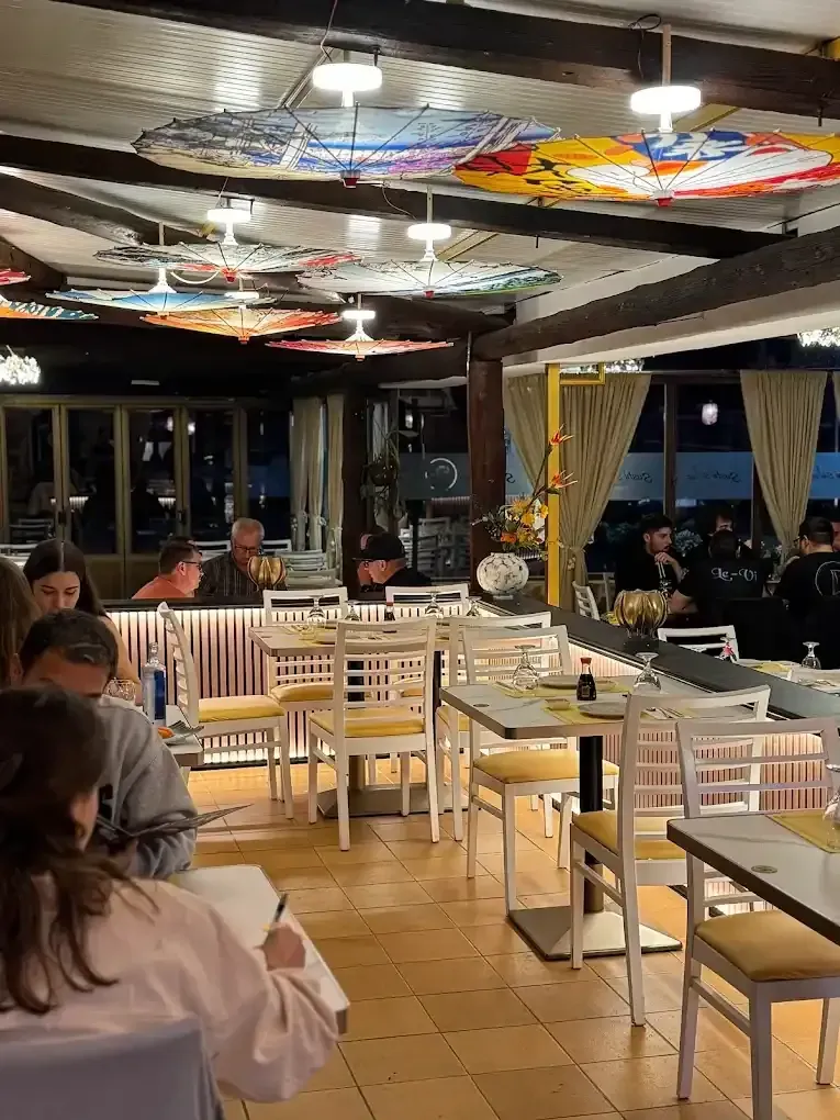 Interior de restaurante con gente cenando. Arte en el techo y sillas amarillas.