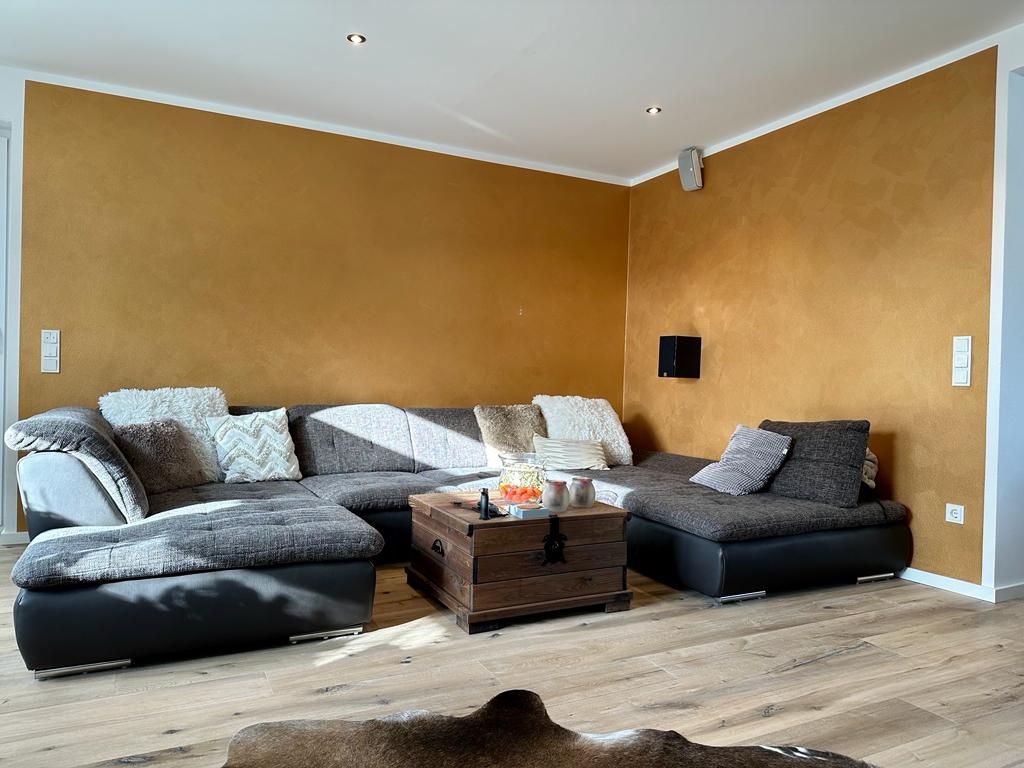 Wohnzimmer mit ockerfarbener Wand und moderner Einrichtung – Farbberatung und Malerarbeit durch die Malerei Segerer.