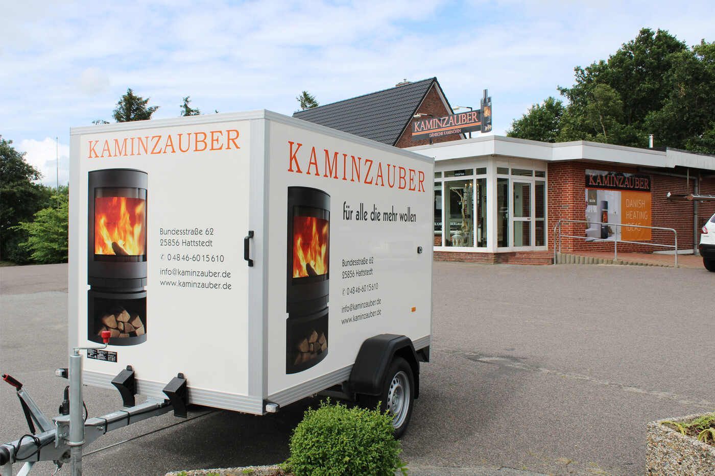 Ein weißer Anhänger steht vor einem Gebäude mit der Aufschrift Kaminzauber