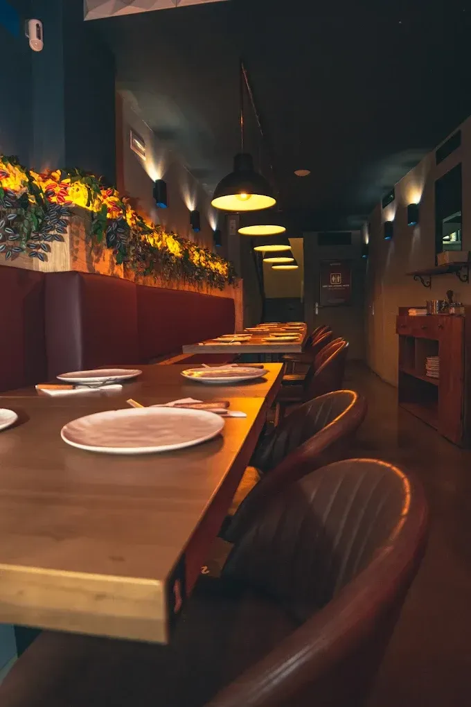 Comedor vacío de un restaurante con mesas de madera, platos y lámparas colgantes cálidas.