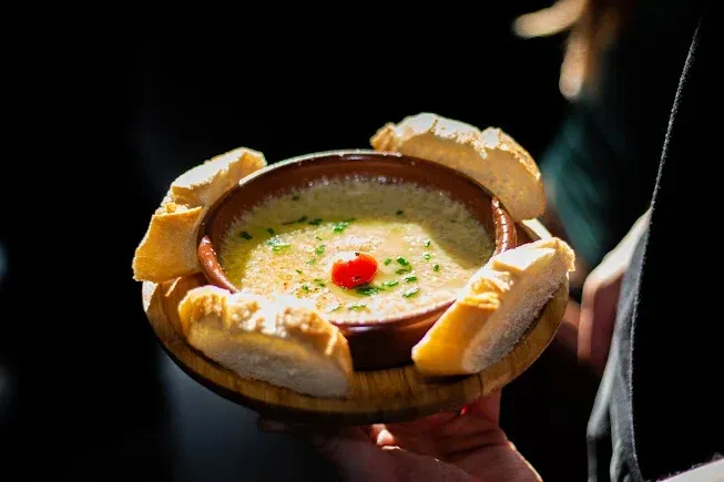 Bol de sopa cremosa para llevar en la mano, con rebanadas de pan alrededor del borde y una guarnición de hierbas.
