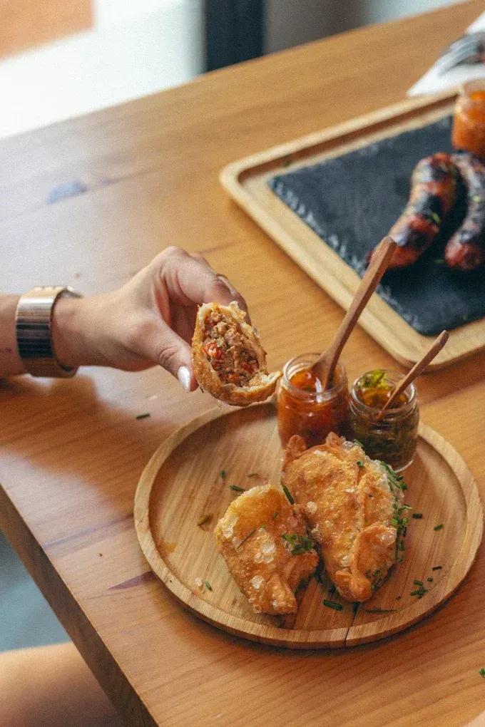 Mojar a mano un bocadillo frito en salsa sobre una mesa de madera con un plato redondo y palillos.