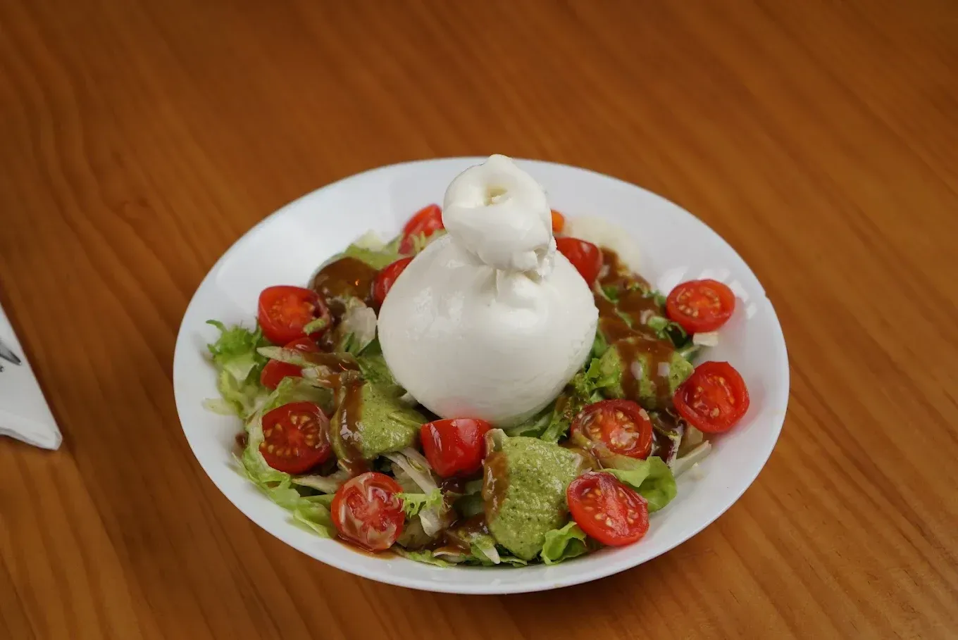 Ensalada con tomates cherry coronada con una bola de queso burrata blanco en un plato.