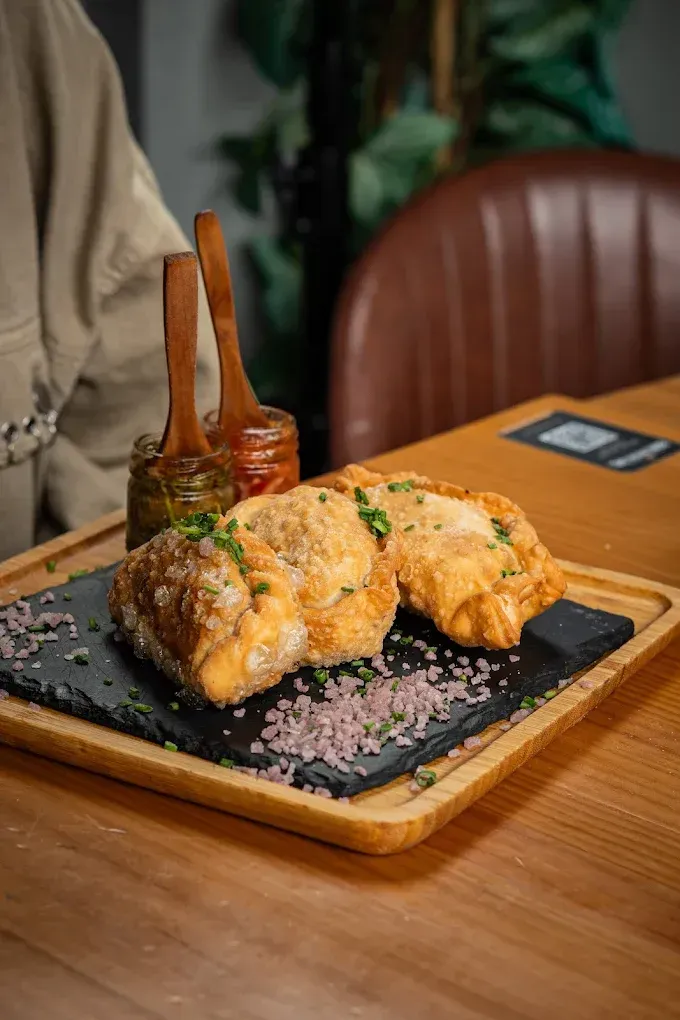Aperitivo frito dorado sobre un plato de pizarra negra con salsa, servido en una mesa de madera.