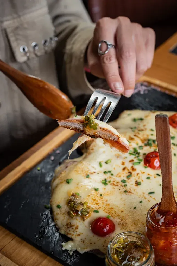 Levantando a mano una porción de pizza con queso de un plato de piedra negra con tomates y hierbas.