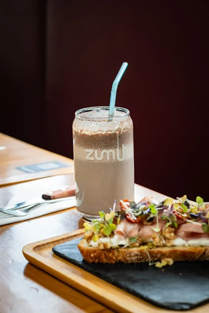 Bebida helada con pajita junto a un sándwich abierto servido en un plato sobre la mesa de un restaurante.
