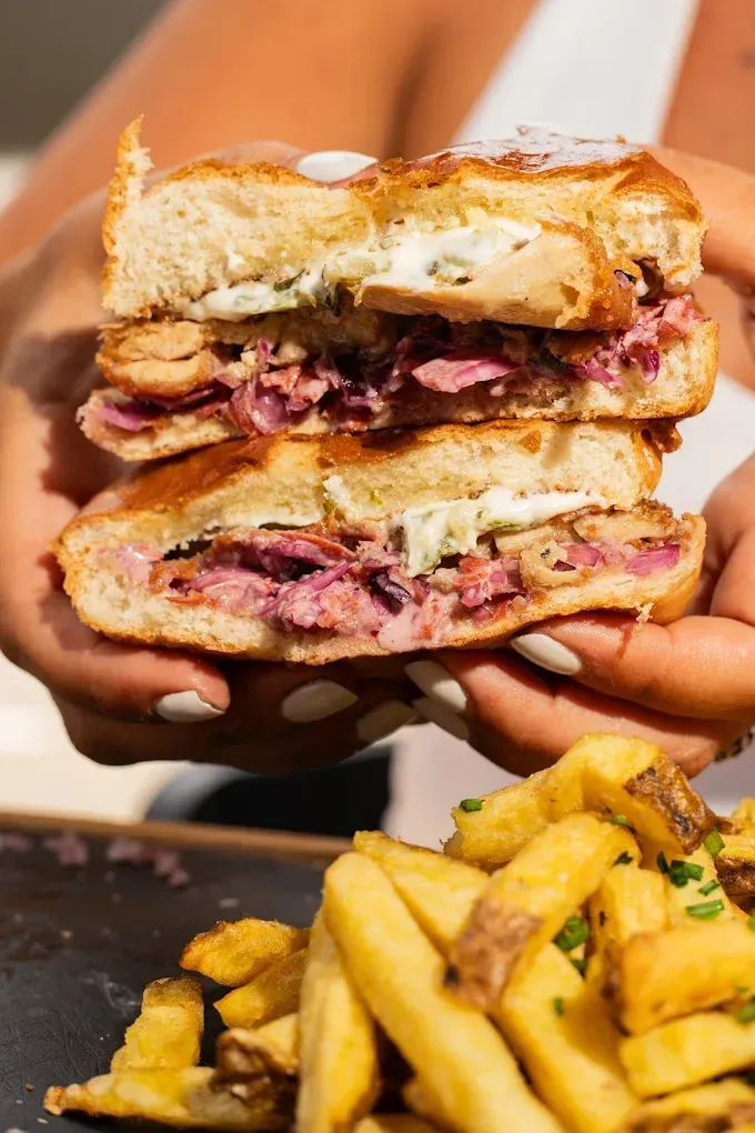 Unas manos sostienen un sándwich partido por la mitad con el relleno derretido.