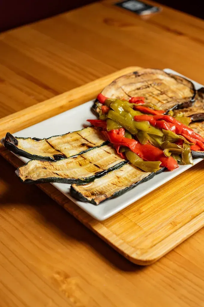 Berenjenas a la parrilla y pimientos asados ​​en un plato blanco sobre una mesa de madera.