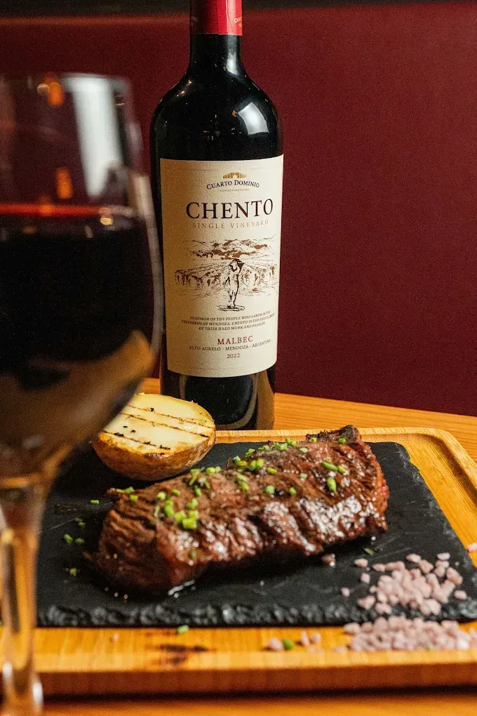 Cena de bistec con botella y copa de vino sobre una mesa de madera en un restaurante.