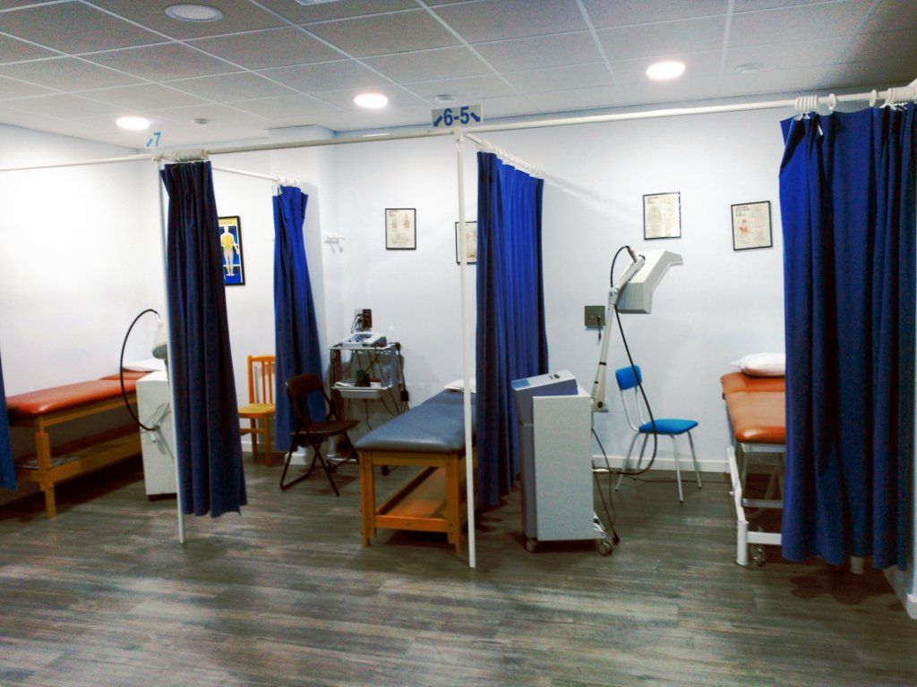Sala de fisioterapia con camillas, cortinas y equipo médico.