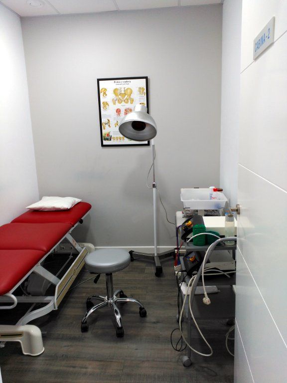 Sala de exploración médica con camilla roja, lámpara, taburete y equipo. Un gráfico de la columna vertebral
