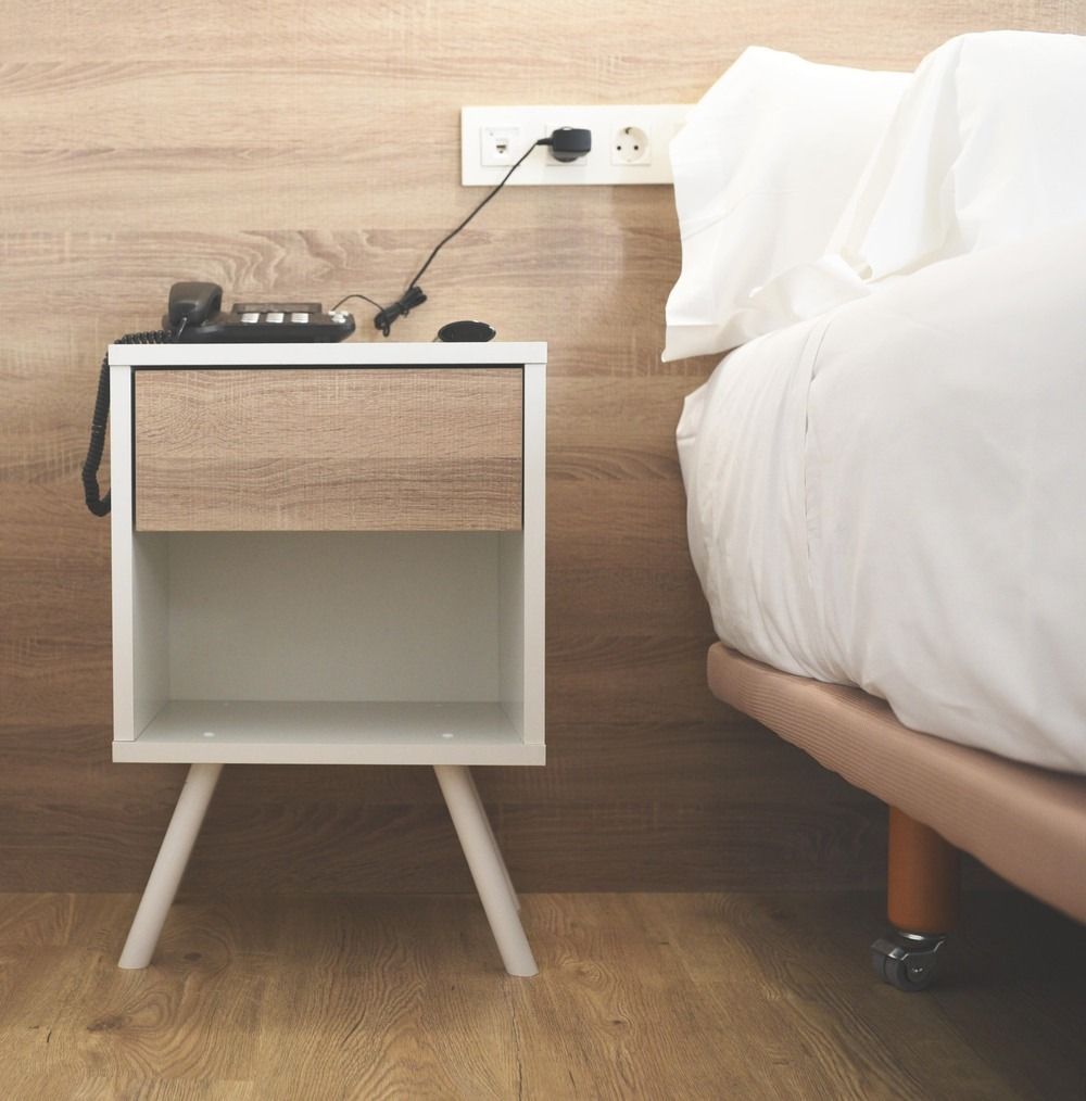 Una mesita de noche con un teléfono encima, al lado de una cama.