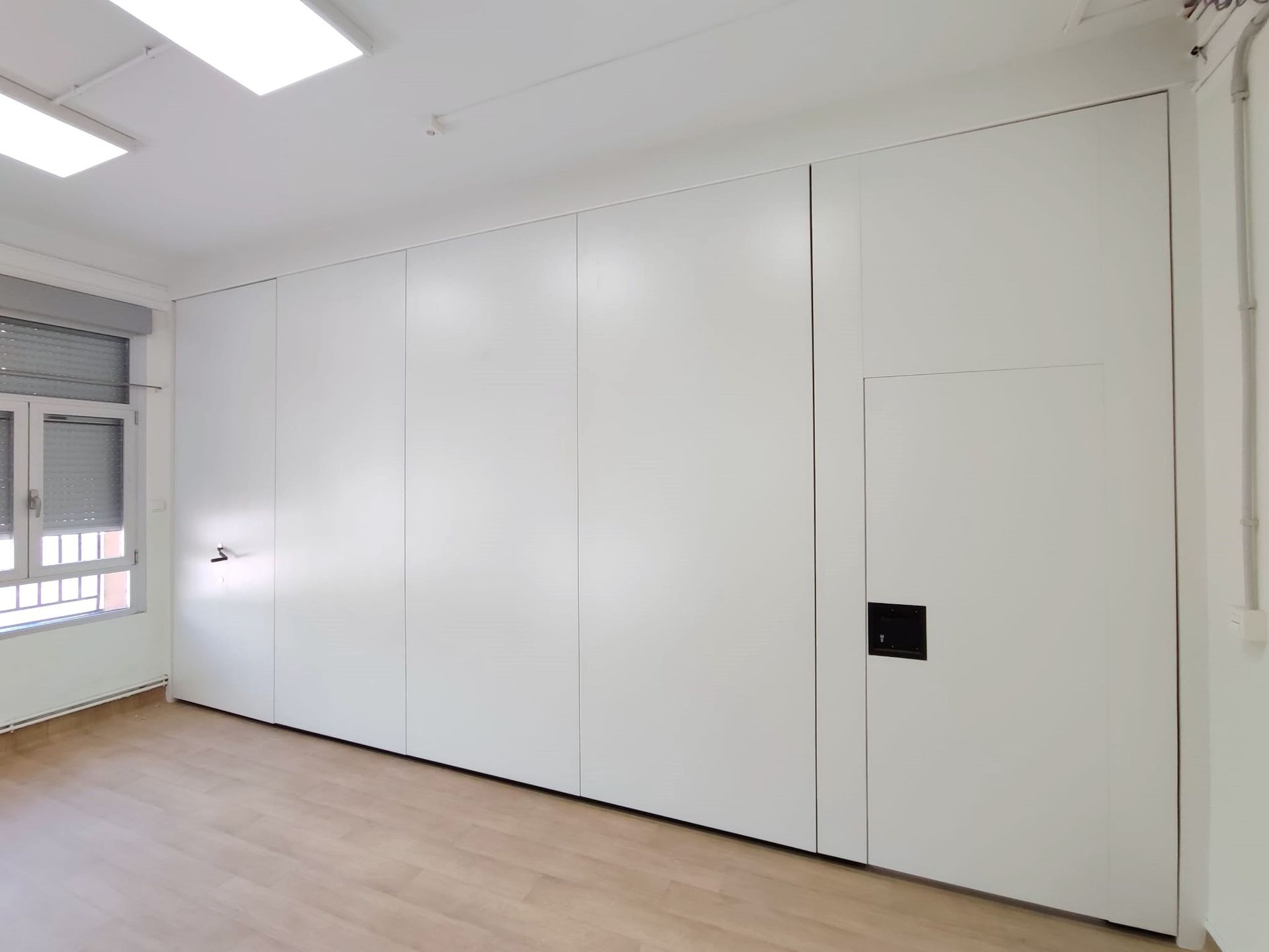 Una habitación con una gran pared blanca y una ventana.