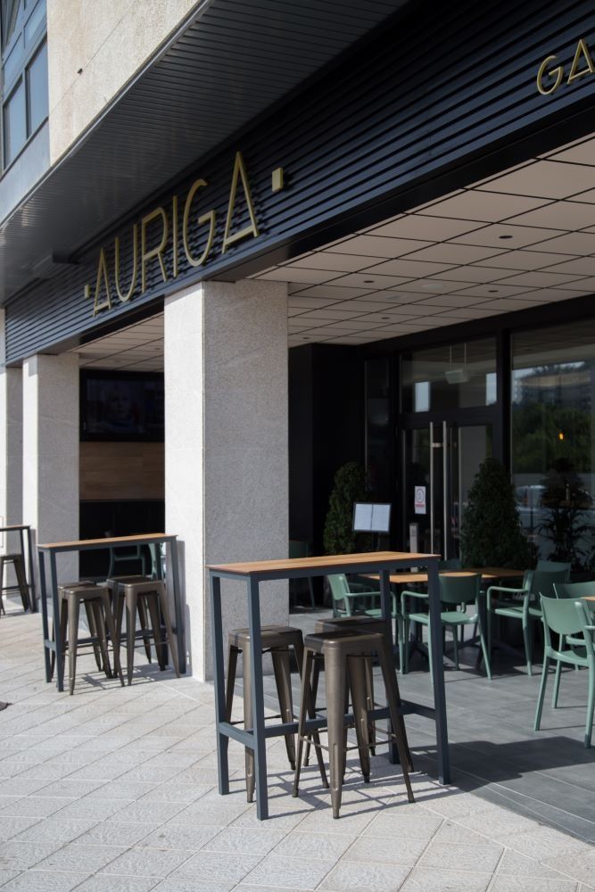 Mesas y sillas afuera de un edificio que dice auriga