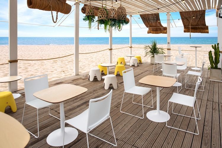 Una terraza de madera con mesas y sillas al lado de una playa.