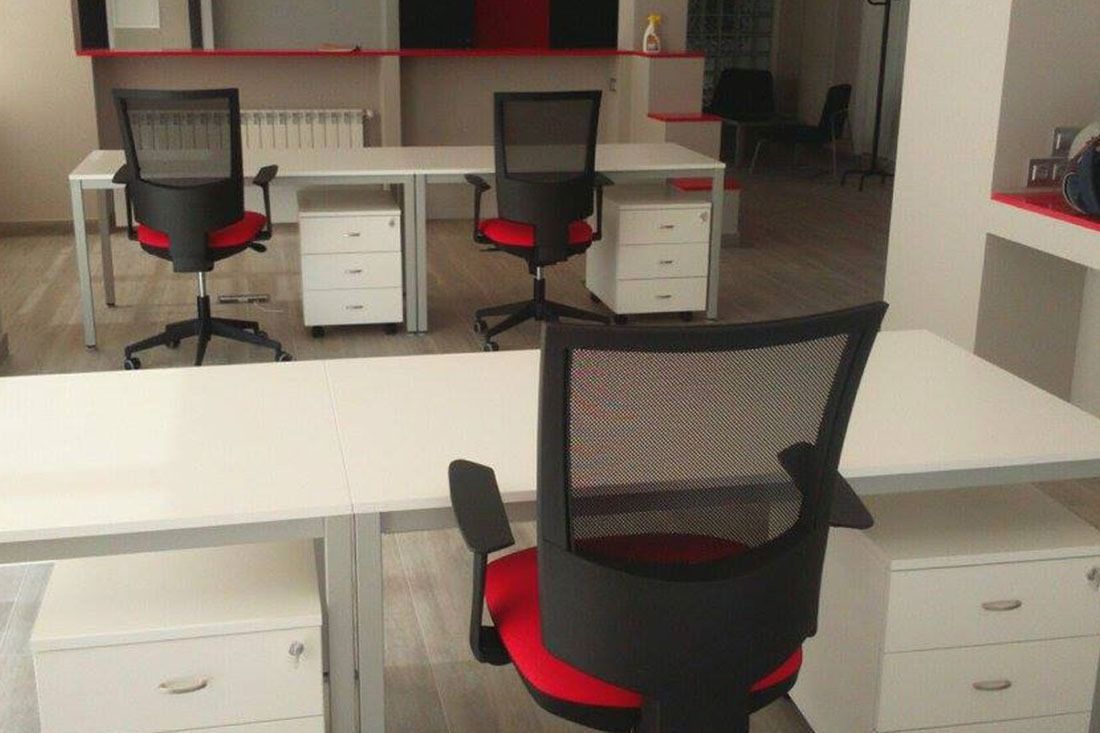 Una silla negra con un asiento rojo se encuentra frente a un escritorio blanco.