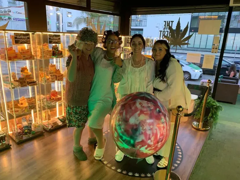 Cuatro personas posan dentro de una tienda cerca de una bola de cristal; los estantes exhiben golosinas.