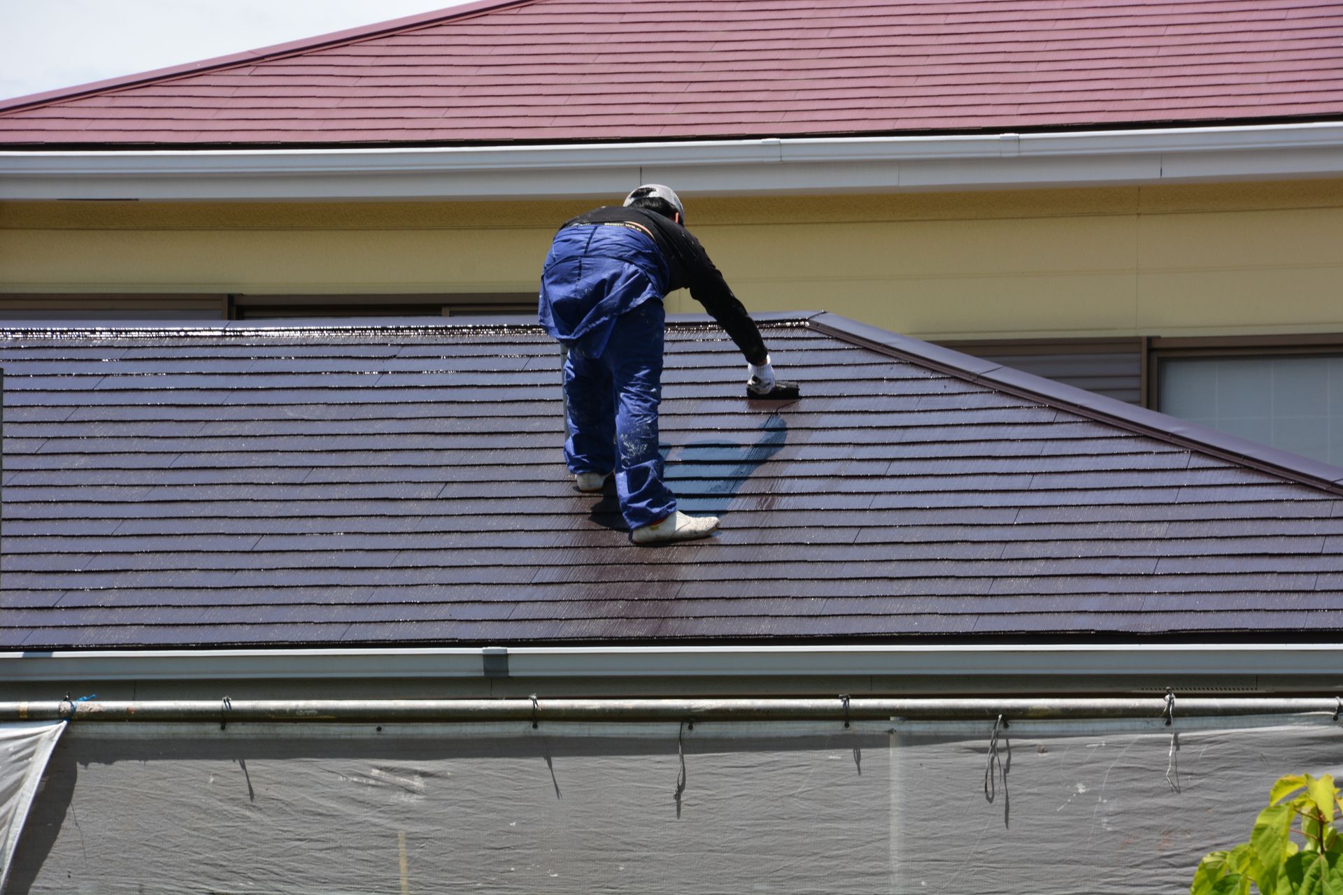 Couvreur appliquant une peinture sur des tuiles depuis le toit d’une maison