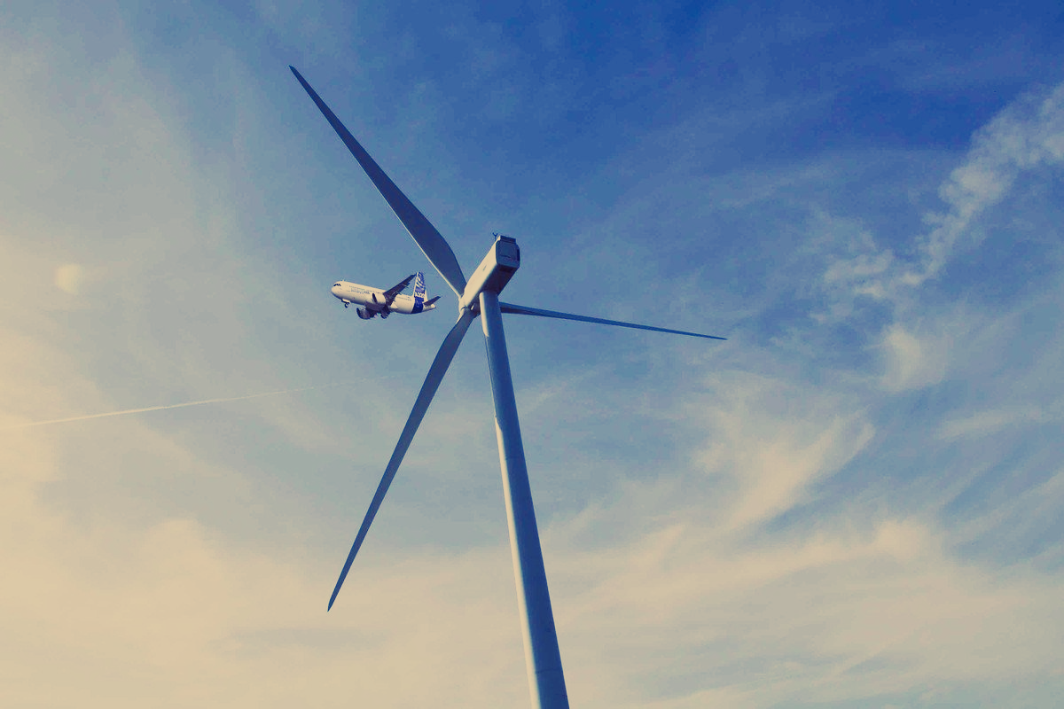 Photo d'un avion survolant une éolienne