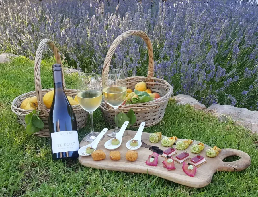 Montaje de picnic con vino, cestas de fruta, entremeses y una tabla de madera para servir en un campo de lavanda.